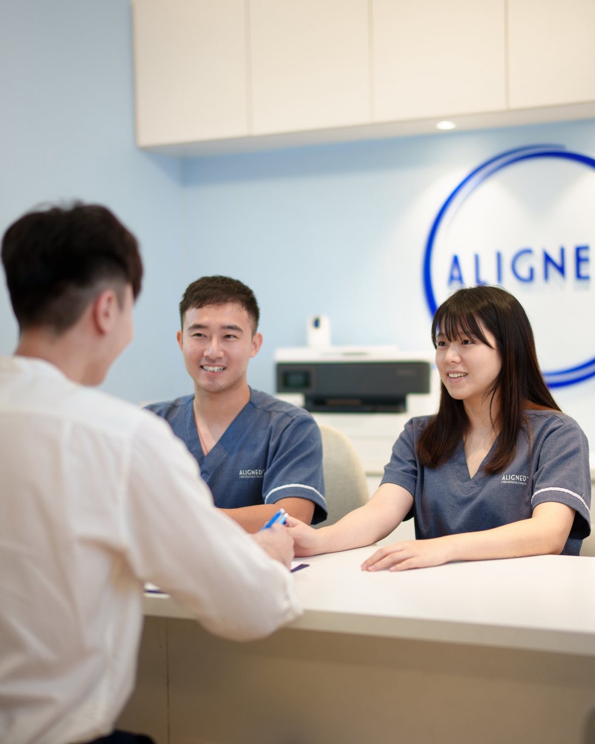 Aligned front-desk team welcoming a patient at the reception counter